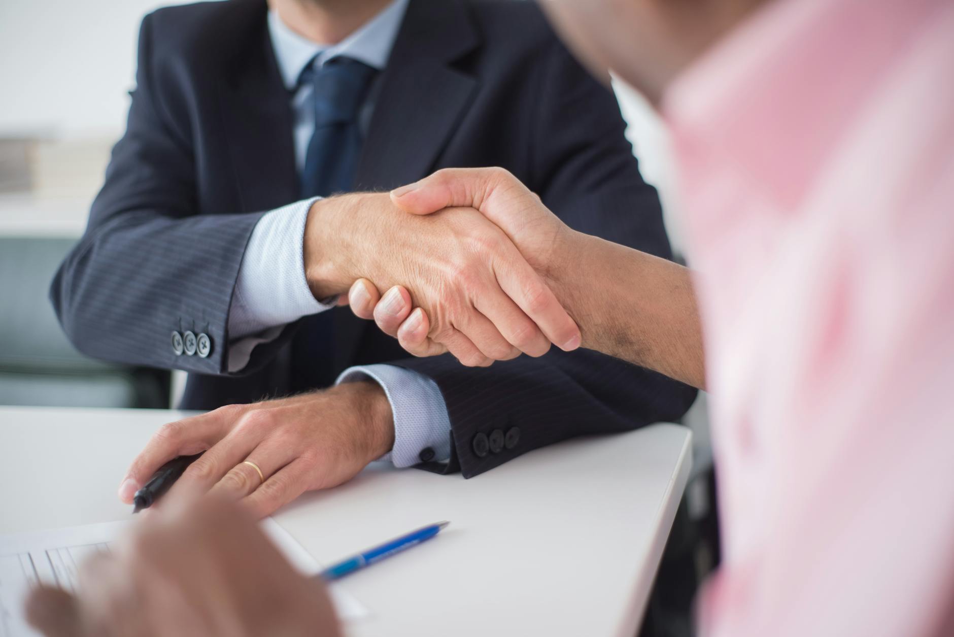 Two businessmen shaking hands across table, symbolizing agreement and partnership in an office environment.